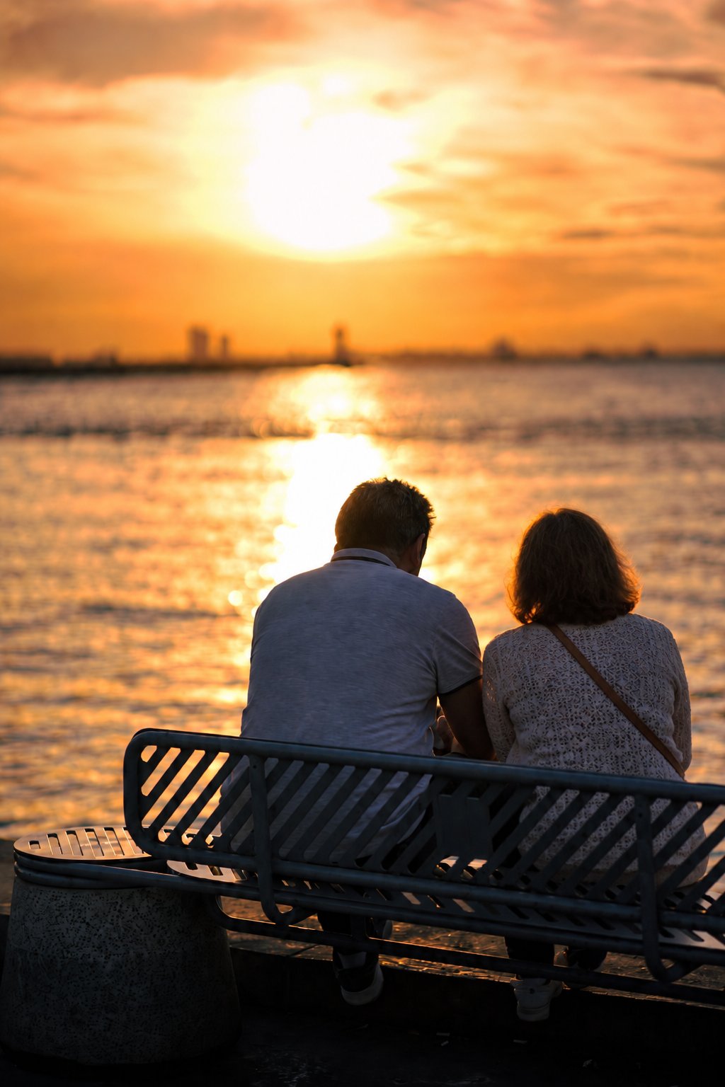 Un couple assis sur un banc face à la mer, au coucher du soleil